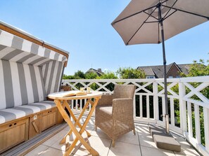 En terrasse med en polstret bænk, en fletstol og et bord med en bog og en kop.