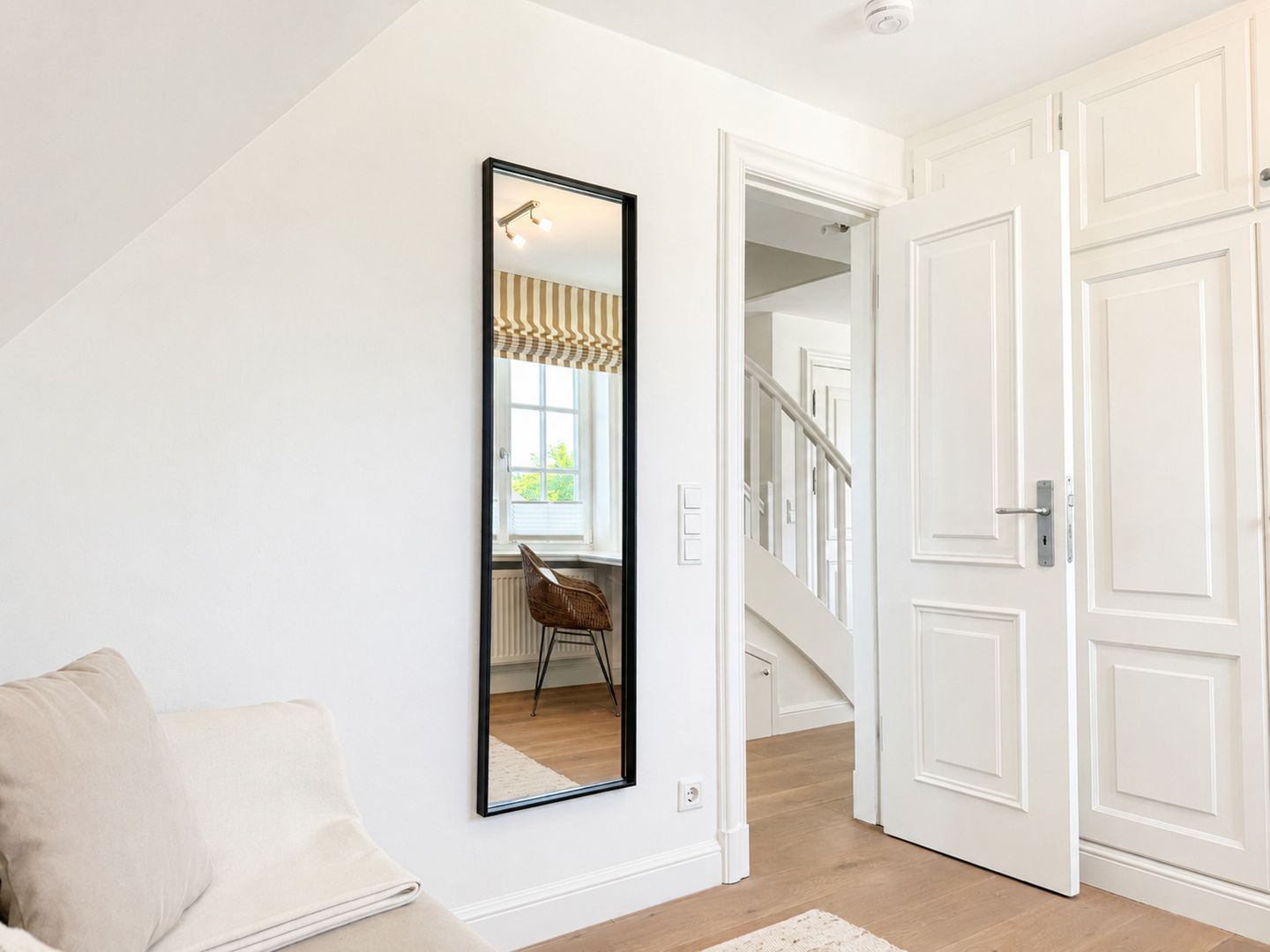 A hallway with a large mirror, a staircase, and a door leading to another room.
