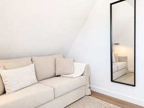 En moderne, minimalistisk stue med en beige sofa, et stort spejl og en enkel gulvlampe.