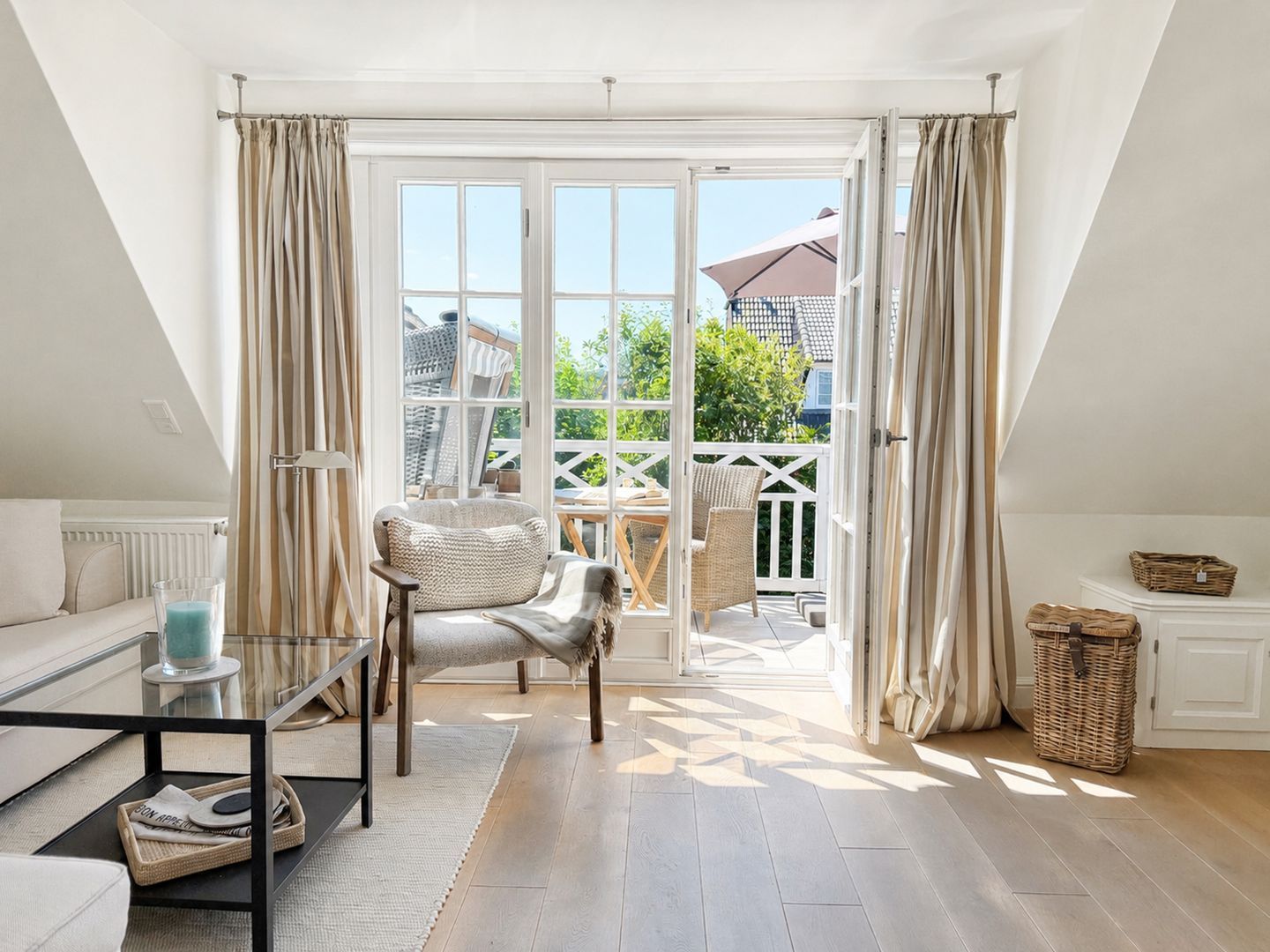 Una habitación con sofá, una silla, una mesa de vidrio y vista al exterior por una ventana grande.