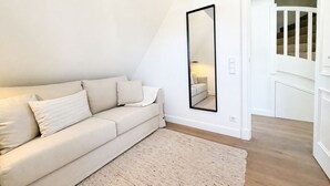 Et værelse med en beige sofa, et stort spejl og trægulv.