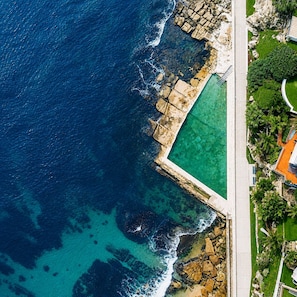 Vista aérea de una propiedad costera con piscina, un muro de piedra y un camino pavimentado.