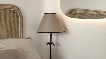 Een bed met een ribbelige witte dekbedovertrek, een lamp met een gevlochten kap en een ronde spiegel aan de muur.