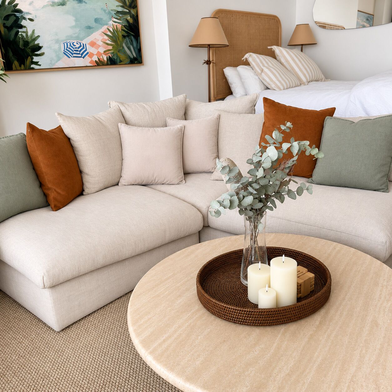 Ein modernes Wohnzimmer mit einem beigefarbenen Ecksofa, einem runden Couchtisch mit Kerzen und einer Korbtischplatte.