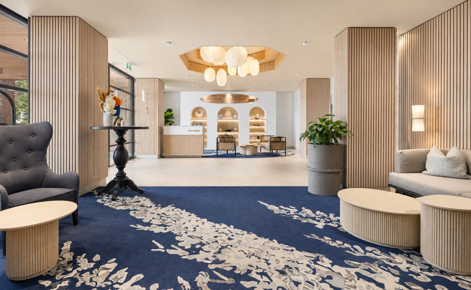 Een moderne hotellobby met een receptiebalie, zithoeken en een decoratieve plafondlamp.
