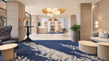 Een moderne hotellobby met een receptiebalie, zithoeken en een decoratieve plafondlamp.