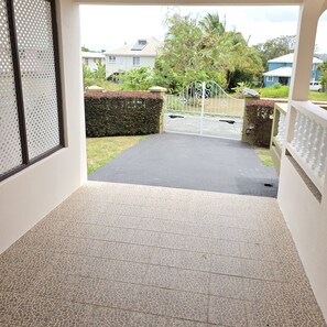 A covered outdoor area with a tiled floor, a metal gate, and a hedge.