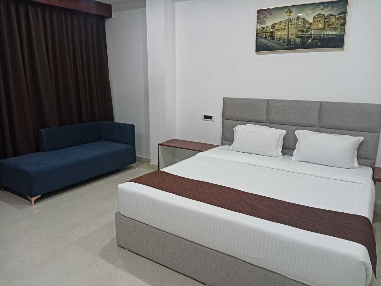 A hotel room with a bed, a blue sofa, a nightstand, and a painting on the wall.