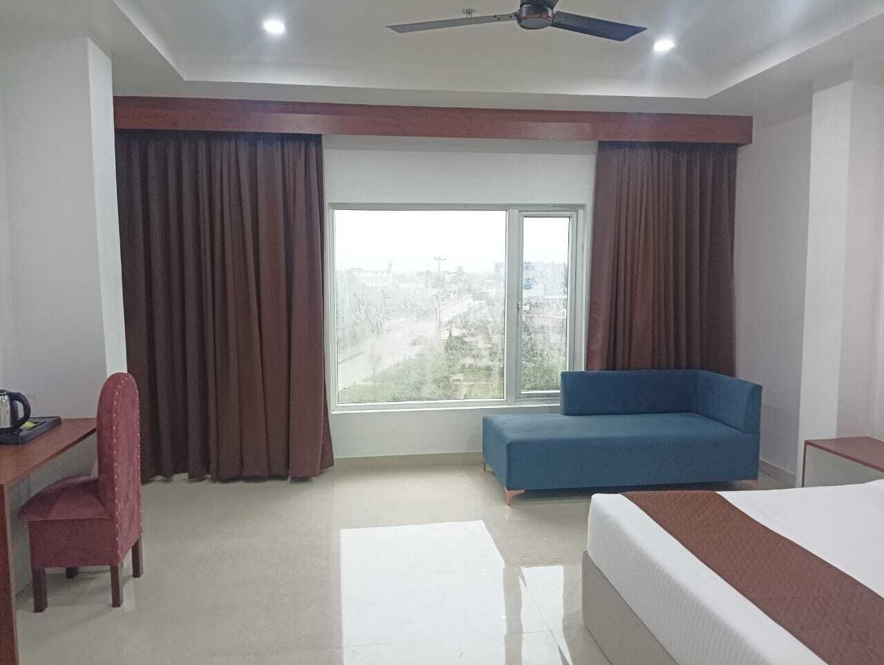 A hotel room with a bed, a desk with a chair, a blue sofa, and a large window with curtains.