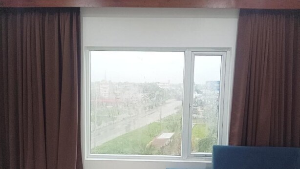 A room with a large window, a blue sofa, and brown curtains. - Hotel RKD Inn (Guwahati)