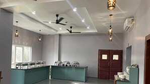 A spacious room with a central island counter, ceiling fans, pendant lighting, and a large window. - Hotel RKD Inn (Guwahati)