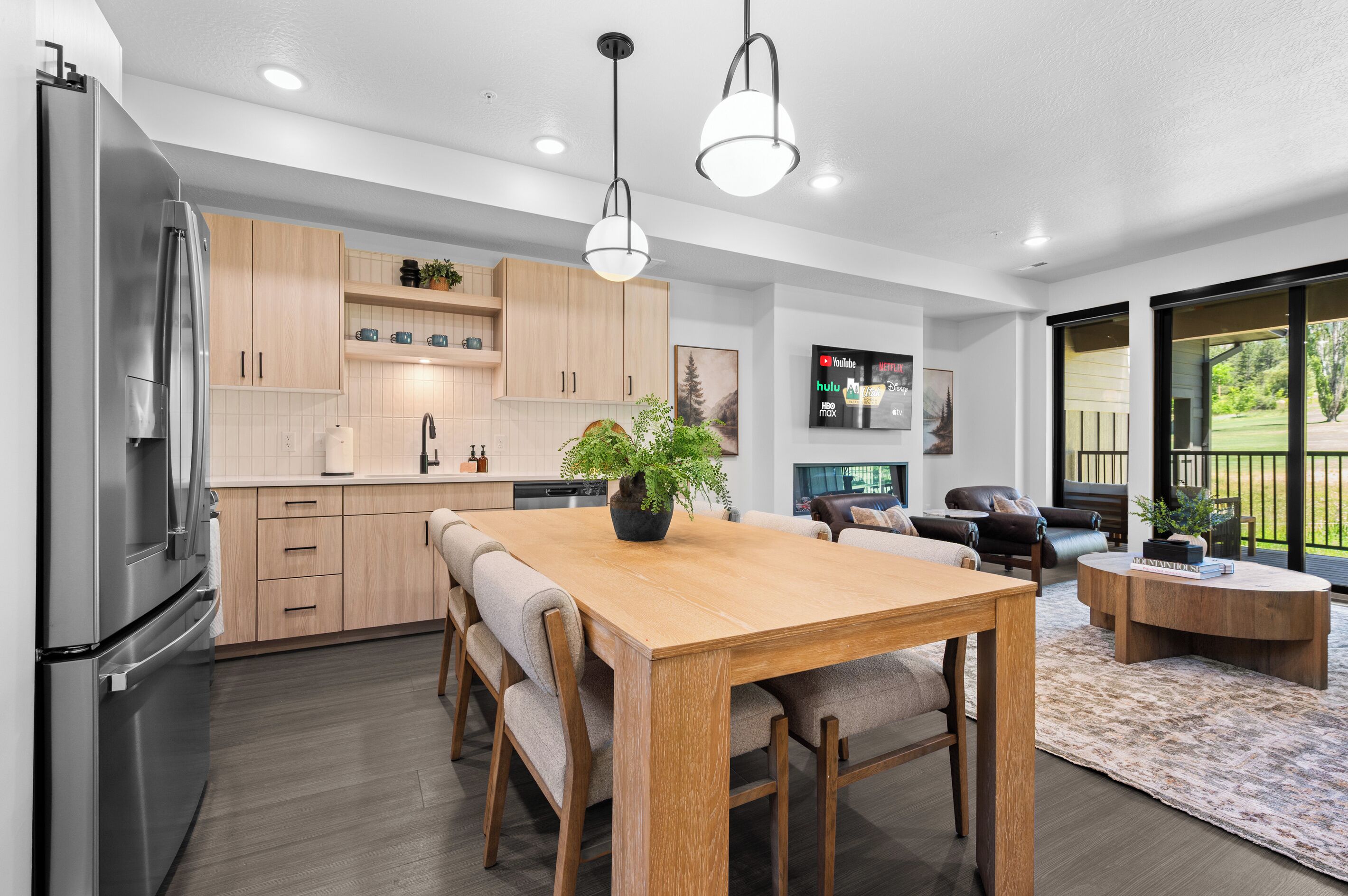 A modern kitchen with a dining area, wooden cabinets, and a large window overlooking a garden.