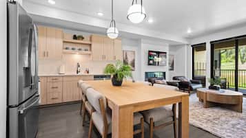 A modern kitchen with a dining area, wooden cabinets, and a large window overlooking a garden.