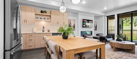 A modern kitchen with a dining area, wooden cabinets, and a large window overlooking a garden.