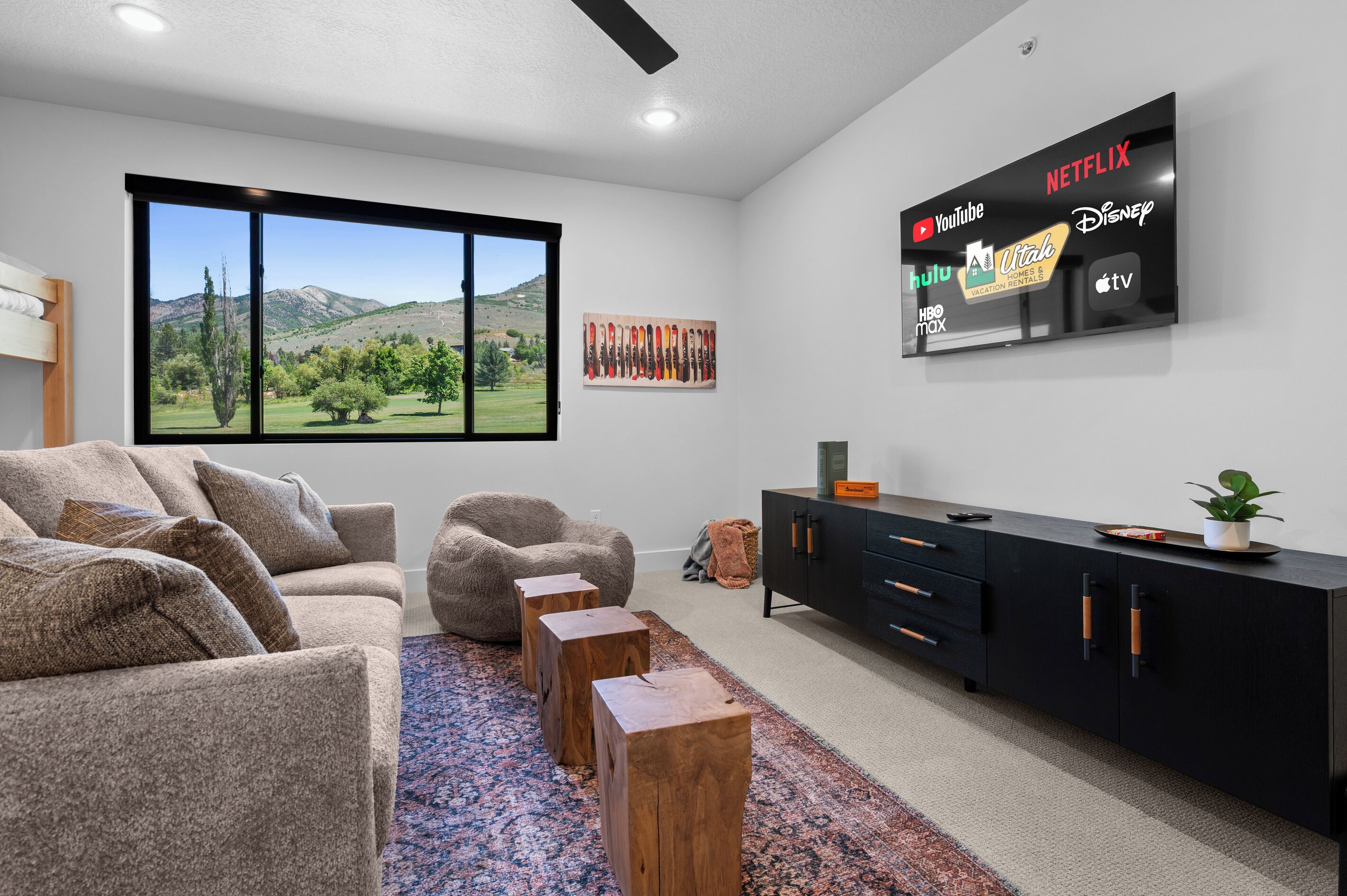 A modern living room with a large window, a black entertainment unit, and a flat-screen TV displaying various streaming services.