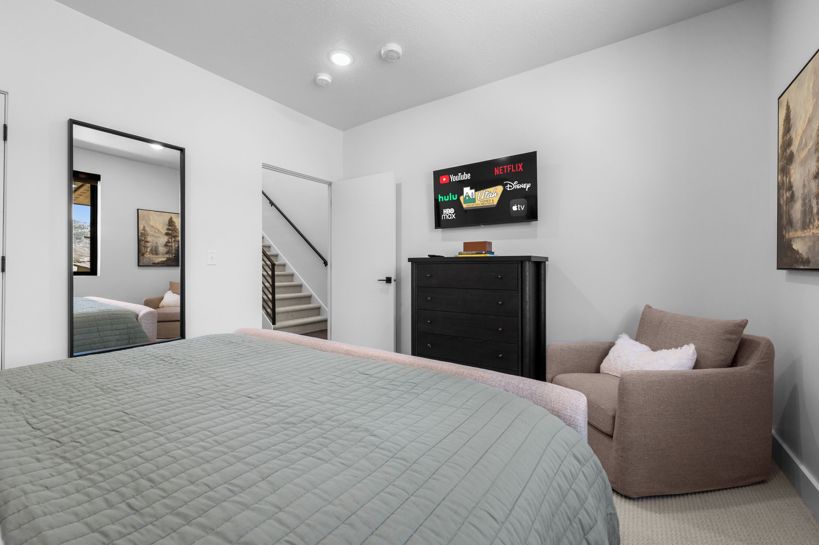 A bedroom with a bed, a dresser, a chair, and a TV displaying streaming services.