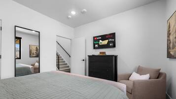 A bedroom with a bed, a dresser, a chair, and a TV displaying streaming services.