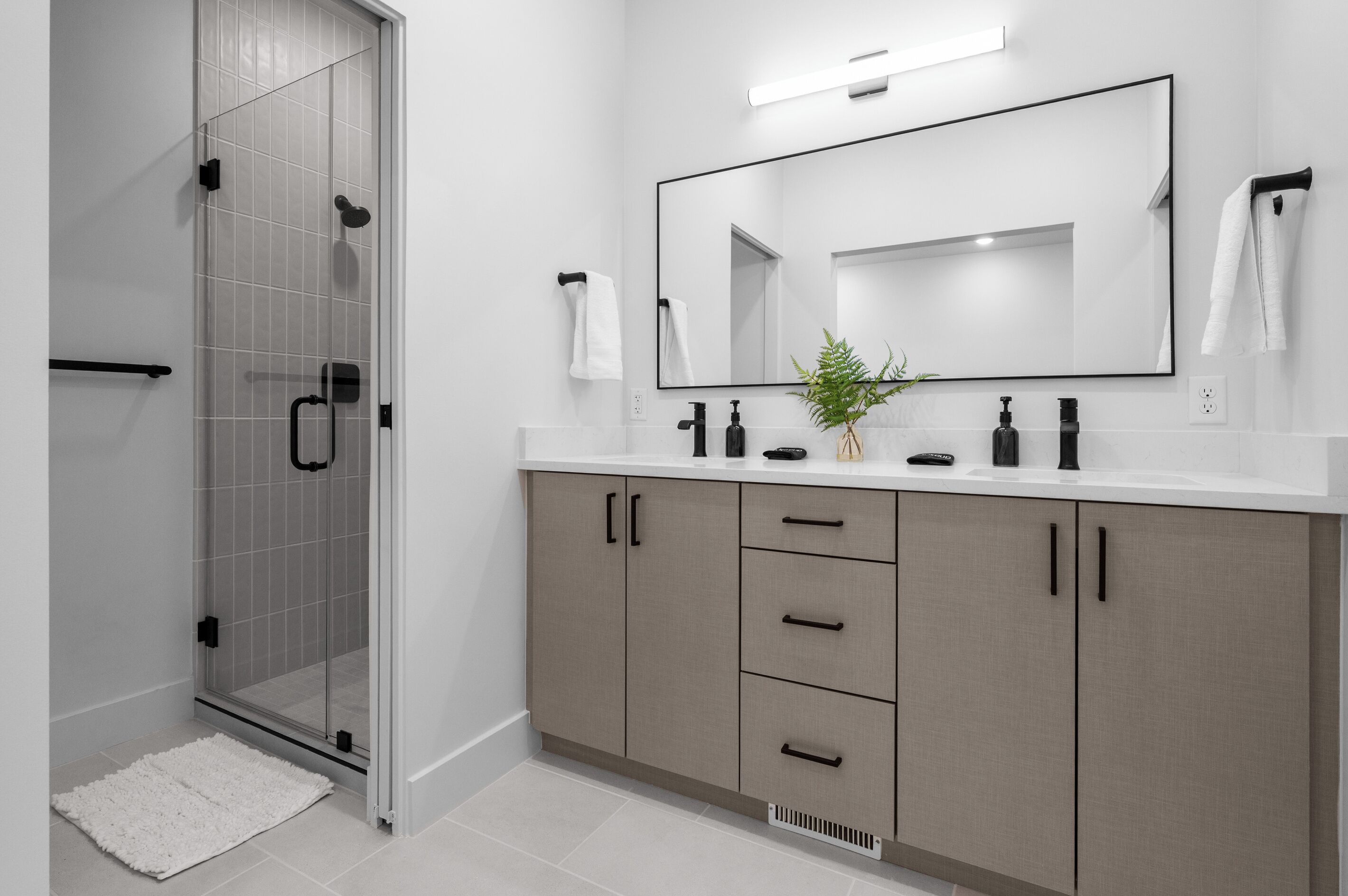 A modern bathroom with a glass shower enclosure, a large mirror, and a vanity with cabinets and drawers.