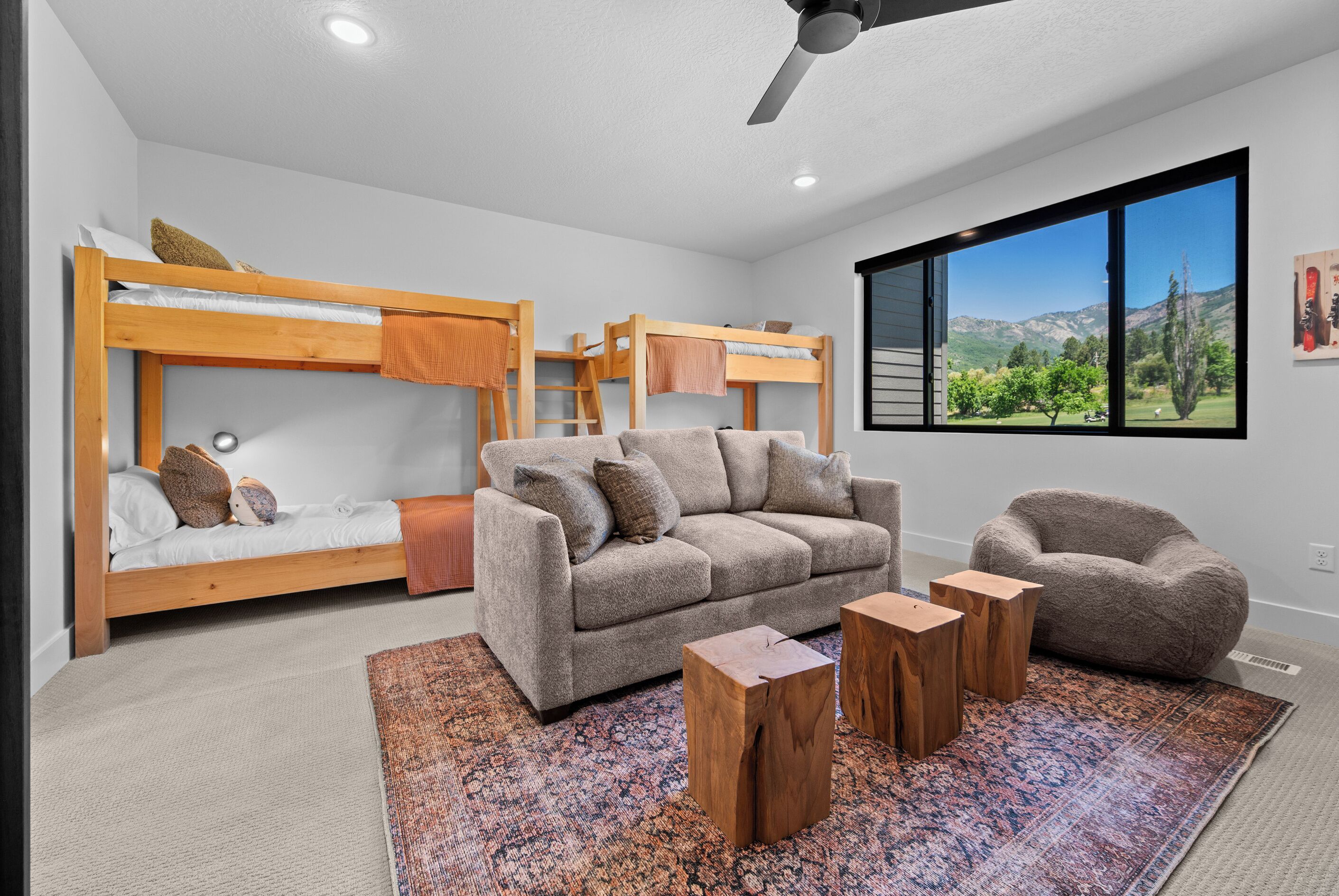 A modern bedroom with bunk beds, a sofa, a chair, and a large window with a mountain view.