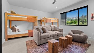 A modern bedroom with bunk beds, a sofa, a chair, and a large window with a mountain view.