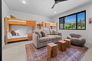 Un dormitorio moderno con literas, un sofá, una silla y un ventanal con vistas a la montaña.