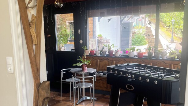 A room with a foosball table, a table with chairs, and a window with plants. - COTTAGE IN THE GERARDMER AREA, SURROUNDED BY NATURE (Ban-sur-Meurthe-Clefcy)