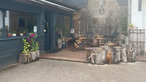 A rustic outdoor seating area with wooden tables and chairs, surrounded by potted plants and tree stumps. - COTTAGE IN THE GERARDMER AREA, SURROUNDED BY NATURE (Ban-sur-Meurthe-Clefcy)