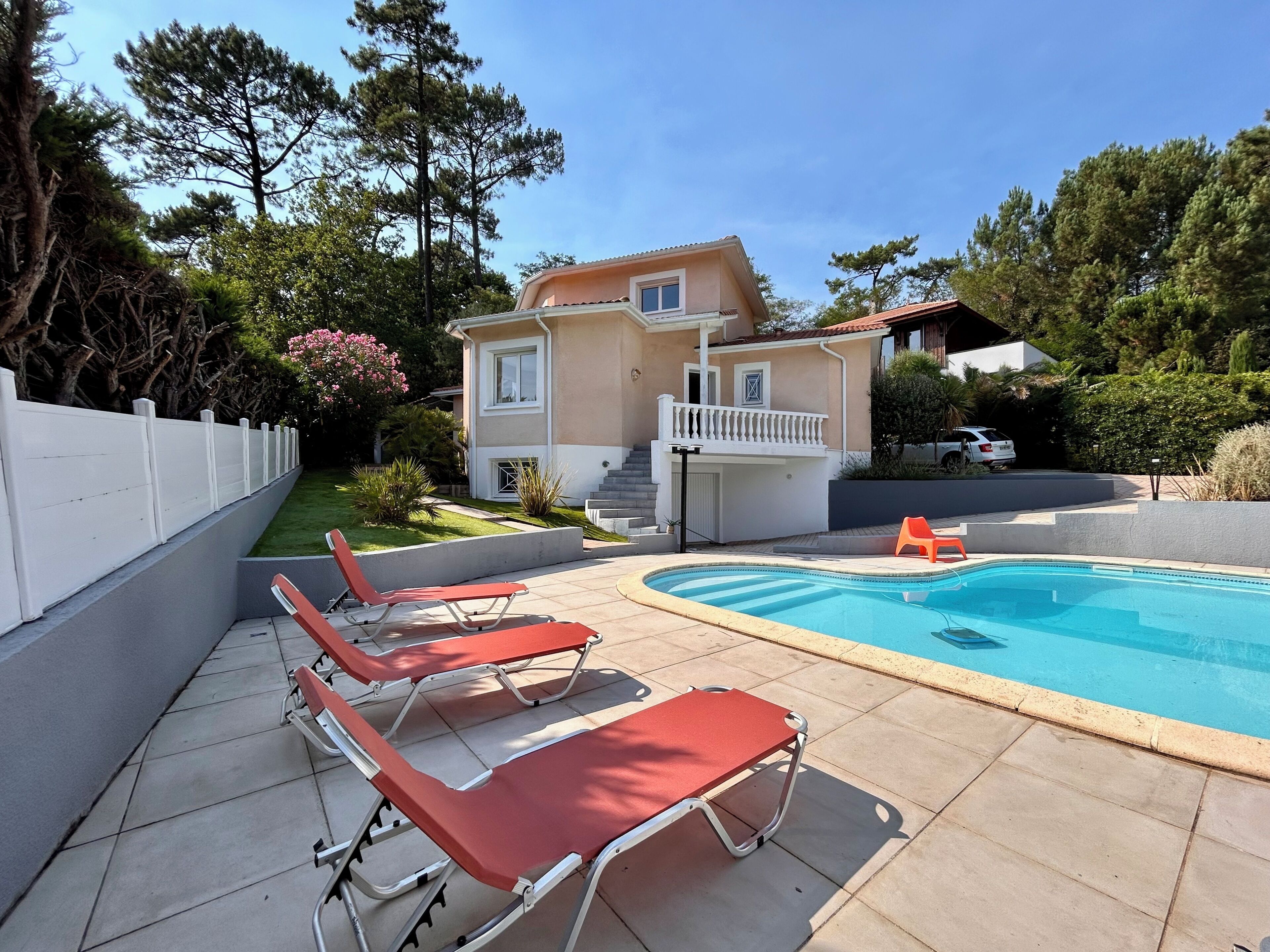 Une propriété résidentielle dotée d’une piscine, de chaises longues et d’une maison à deux étages.