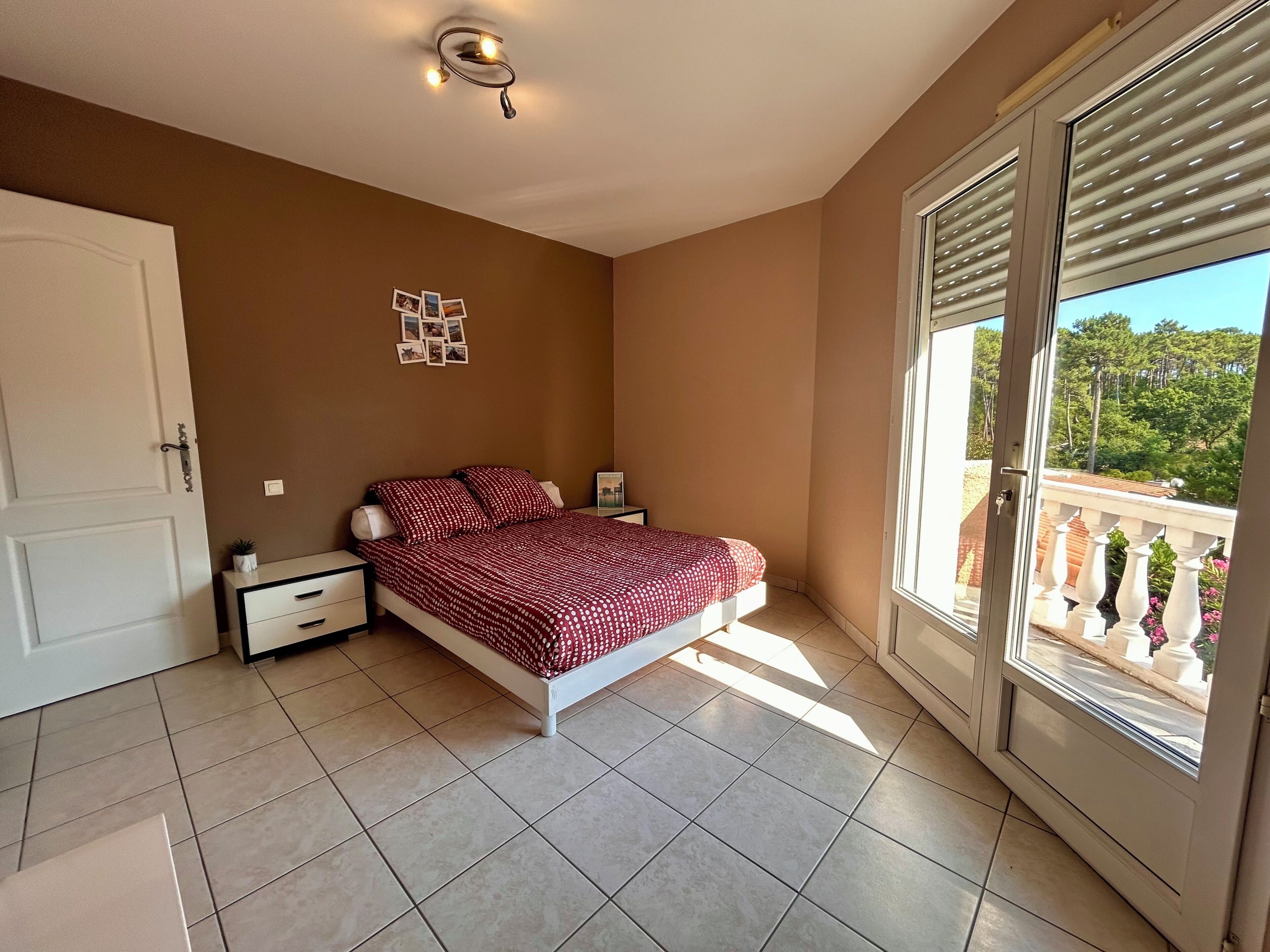 Une chambre à coucher comprenant un lit, une table de chevet, une commode, un tableau accroché au mur et une porte-fenêtre coulissante donnant sur un balcon.
