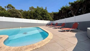 Ein Schwimmbad mit gefliestem Sonnendeck und roten Liegestühlen.