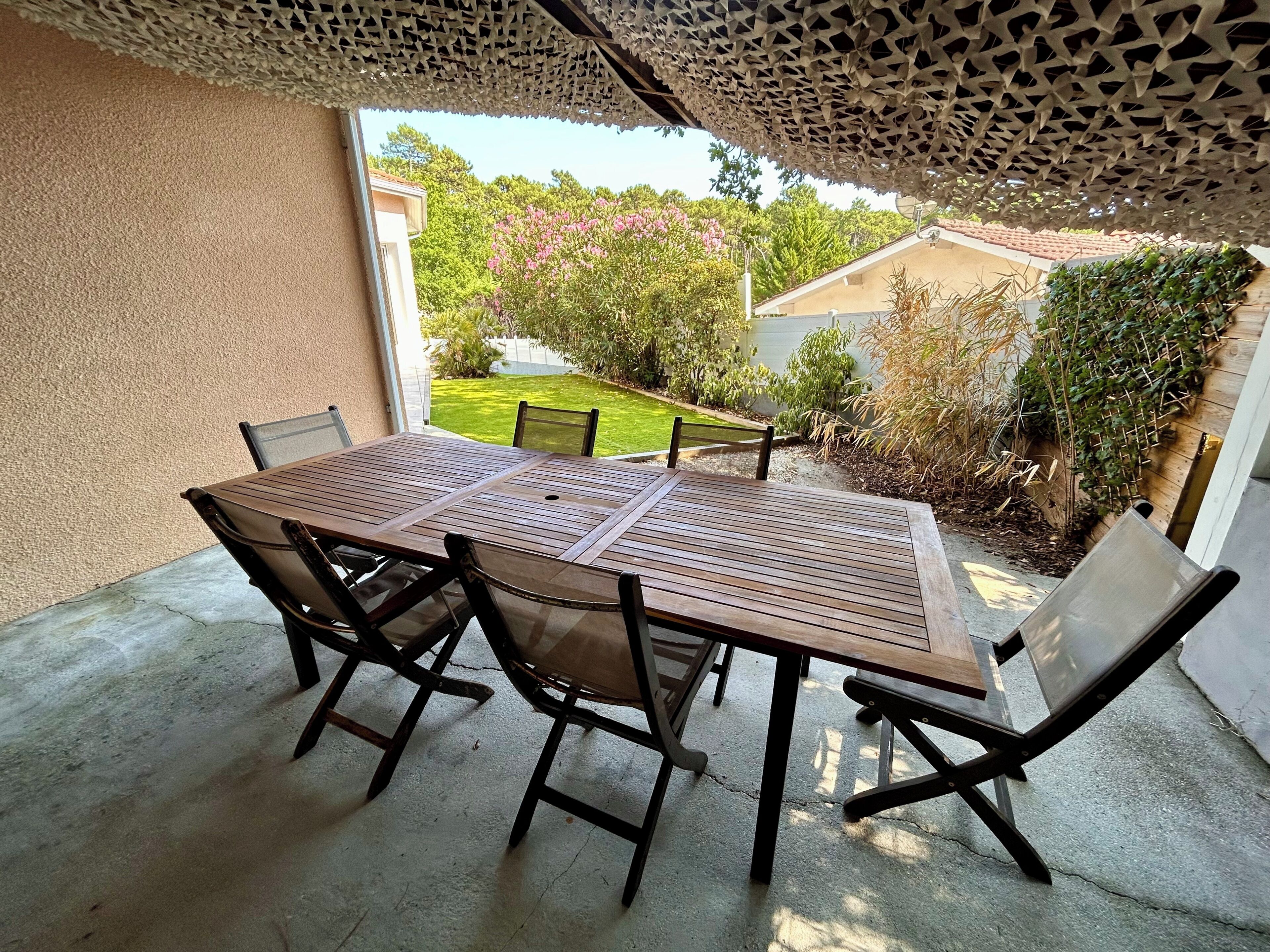 Una veranda esterna con tavolo e sedie, vista su un giardino e una casa sullo sfondo.