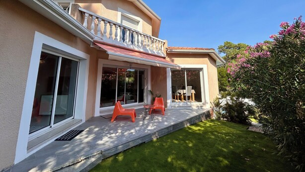 Ein Haus mit überdachter Terrasse, großen Fenstern und einem gepflegten Rasen.