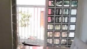 Ein Essbereich mit Tisch und zwei Barhocker, einer Couch und Blick durch ein Fenster mit Metallgitter.
