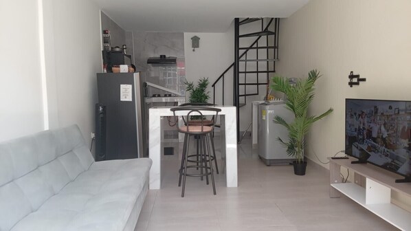 Un espai vital reduït amb bugateria, zona de dinar, sofà, televisor i escala.