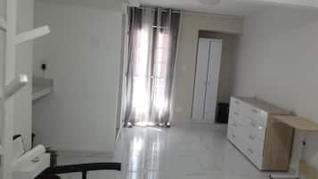 A spacious room with a large window, a wardrobe, and a wooden cabinet.