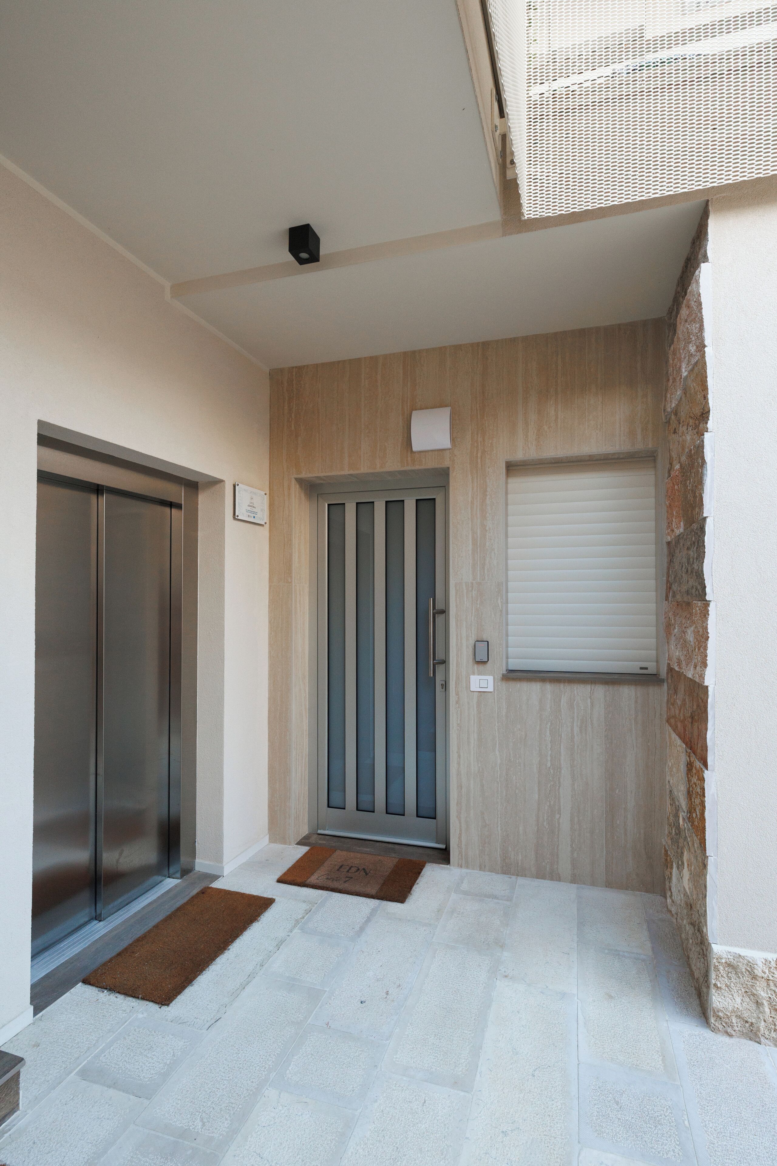 Une entrée moderne avec une porte, une petite fenêtre et un portail en métal.