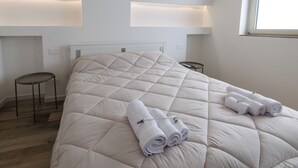 Una cama bien tendida con toallas enrolladas y un control remoto sobre la mesita de noche.