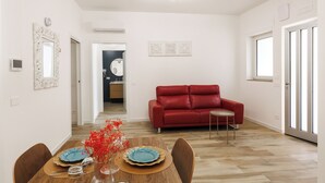 Un comedor con una mesa de madera dispuesta para dos personas, un sofá rojo y una mesita auxiliar.