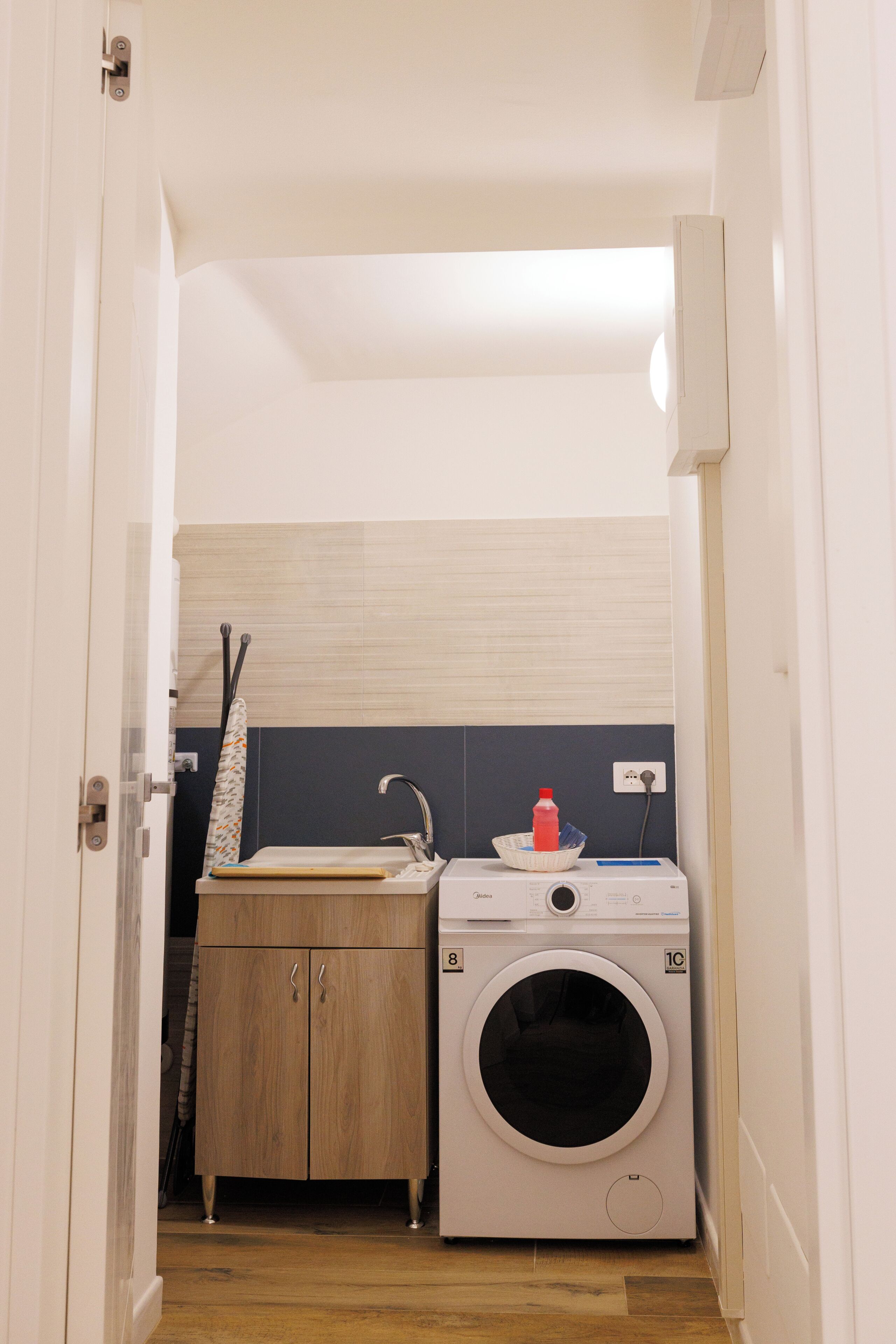 Une petite buanderie équipée d’un lave-linge, d’un évier et d’un meuble en bois.