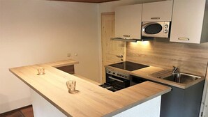Ett kompakt kök med en central köksö, en mikrovågsugn, en ugn och en diskho.