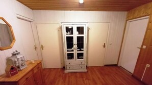 En hall med trägolv, ett vitt skåp med glasdörrar och en spegel på den vänstra väggen.