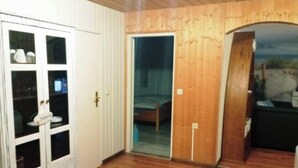 Ett rum med trägolv, en säng, en vit dörr med glaspaneler och ett litet fönster.