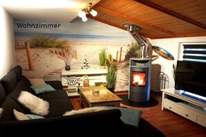 Ein gemütliches Wohnzimmer mit Kamin, einer Couch, einem Fernseher und einem Wandbild mit Strandmotiv.