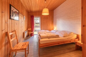 Una habitación con paneles de madera, una cama, una silla, una mesa y una lámpara colgante.