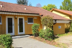 A two-story building with a tiled roof, a front door, and a small attached structure with a parking sign. - Urlaub im Grünen - Doppelbungalow mit Terrasse im Ferienpark Mirow (Granzow)