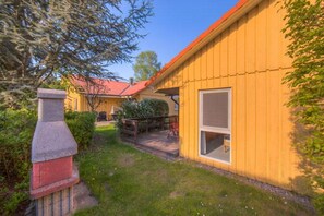 A yellow wooden building with a red roof, a stone chimney, and a small porch. - Urlaub im Grünen - Doppelbungalow mit Terrasse im Ferienpark Mirow (Granzow)