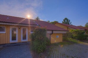 A building with a tiled roof, a paved driveway, and a parking sign. - Urlaub im Grünen - Doppelbungalow mit Terrasse im Ferienpark Mirow (Granzow)