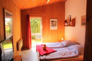 Una habitación de madera con dos camas, una ventana con cortinas e imagen enmarcada en la pared.