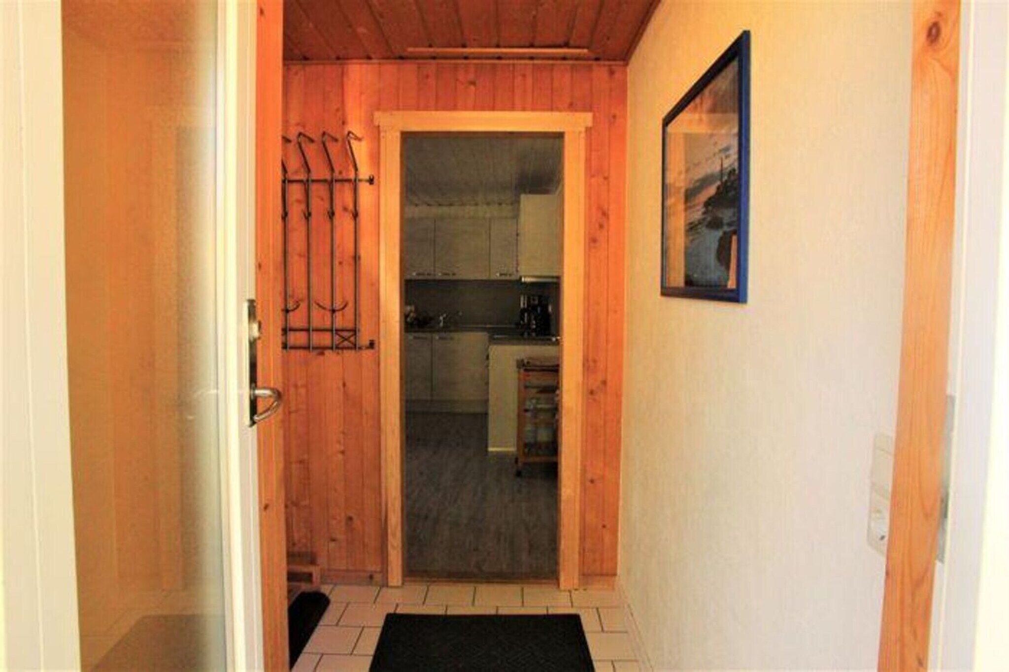 A wooden interior hallway leading to a kitchen with cabinets and a door.