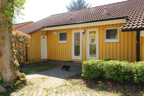 A yellow building with a tiled roof, a paved driveway, and a small garden area. - Urlaub am Wasser - Doppelbungalow mit Terrasse im Ferienpark Mirow (Granzow)